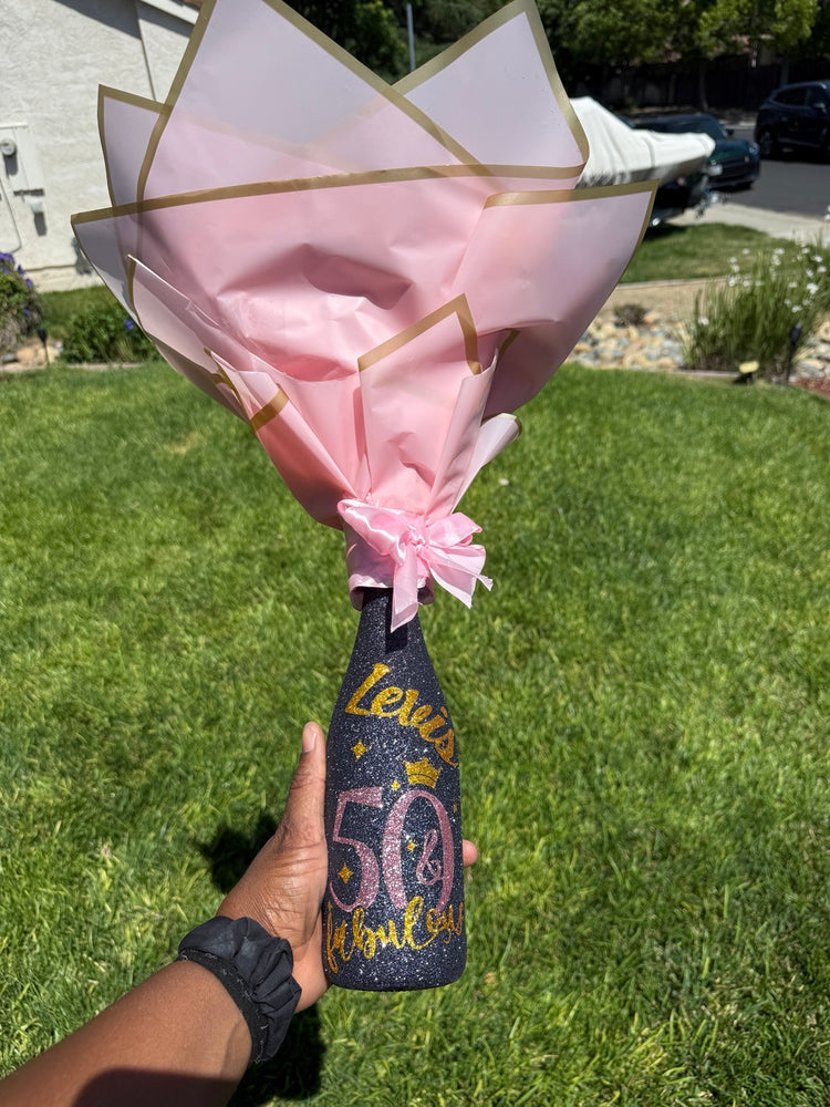 Personalized glitter bottle topped with a wrapped flower bouquet, pink ribbon, and heart balloon accent